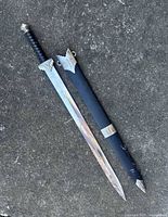 Vintage Viking style sword with black handle and metal pommel and guard, laying next to a black scabbard with metal fittings.