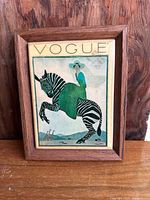 Front view of the framed Vogue wall tile showing the vintage illustration of a woman in green dress riding a striped zebra.