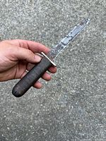Holding close-up image of a rusted World War I trench cutter knife with wrapped handle and metal guard.