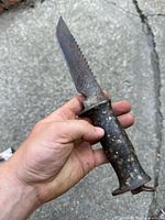 Front side of the knife showing blade shape, serrated edge and stacked leather handle with patina.