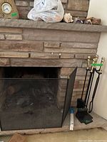 Fireplace with black mesh protector screen and five-piece fireplace tool set with brass handles and black cast iron tools on the side.