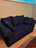 Front view of dark blue loveseat sofa with cushions on hardwood floor under window.