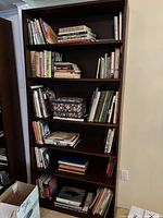 Front view of the wooden bookshelf filled partially with books and a floral patterned case on one shelf.