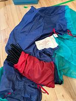Sleeping bags in blue and teal colors with red drawstring bags containing tent poles or support rods