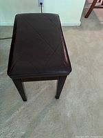 Top view of dark brown faux leather seat on wooden piano bench showing diamond stitching.