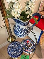 Photo of ceramic pitcher with blue floral design filled with artificial white flowers, alongside two ceramic coasters with intricate Portuguese tile patterns and rooster motif.