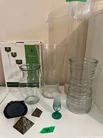 Green glass candle holders in original box, clear glass vases, souvenir glass, and small pyramids displayed on a surface.