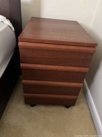 Front side angle view of the wooden desk drawer cabinet showing four horizontal drawers and caster wheels underneath.