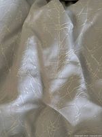 Close-up detail of grey fabric with white embroidered branch pattern on comforter or pillowcase.