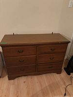 Front view of wood dresser showing six drawers with brass handles, medium brown finish and curved base.