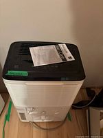 Front top view of the white and black Frigidaire dehumidifier with manual on top.