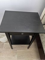 Top view of black night table, showing flat surface with minor scuffs and scratches.