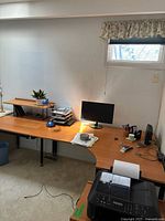Large wooden corner desk in curved design with 3 connected pieces and a raised monitor shelf. Light brown wood finish with black metal legs. Shows some signs of use and includes cable management holes.