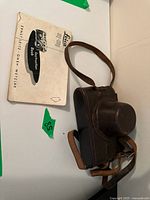 Instruction booklet and brown leather case on white surface