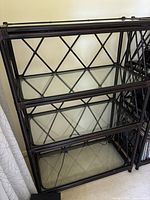Front and side angled views of the metal frame shelving unit with 3 glass shelves showing dark brown finish and crisscross metal side panel design.