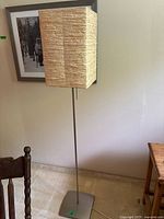 Full view of the floor lamp showing beige rectangular textured paper shade and metal base on carpeted floor.
