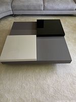 Top-down view showing four square panels in black, grey, dark grey, and white flush on taupe base