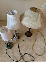 Set of 3 metal table lamps with fabric shades arranged on carpet. Different styles and heights, cords visible.