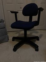 Front view of blue fabric office chair showing cushioned seat and backrest, black plastic armrests, and caster base.