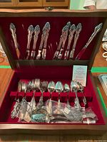 Full view of the Oneida silverware set displayed inside a wooden case with red interior, showing a variety of forks, knives, spoons, and serving utensils.