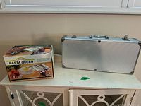 Pasta Queen box beside a silver carrying case containing a Cuisinart kitchen appliance
