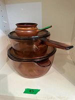 Two Pyrex amber glass cookware pots stacked with lids on a shelf with a small brown ceramic pot on top