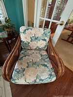 Front view of single rattan chair showing floral seat and back cushions with large flower pattern.
