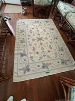 Area rug laid out on wooden floor, showing floral design and pastel colors