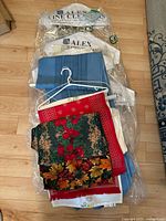 Photo showing a stack of assorted table runners and tablecloths including the ornate blue cloth from Egypt, with multiple floral and patterned designs in various colors.