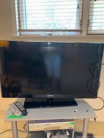 Full front view of Samsung 46-inch flat panel TV on stand with remote control and power cable on table below.