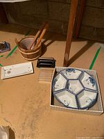 Overall view of the wooden sauna bucket with ladle, porcelain serving pieces, and letter holders all arranged on the floor.