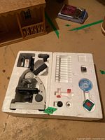 Microscope and laboratory accessories organized in foam packaging on a table.