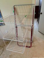 Front and side view of white metal 3-shelf wire grid organizer with laundry drying rack leaning behind.