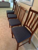 Four teak slat-back side chairs lined up against wall