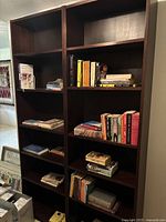 Front view of two dark brown wood particle board bookshelves filled with various books on most shelves.