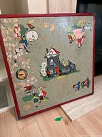 Top view of square vintage metal kids table with painted illustrations and multiple stickers, red edges visible.