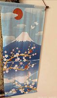 Front view of a vertical Japanese scroll textile wall hanging depicting Mt. Fuji, cherry blossoms, sun and birds on a blue sky background hung on a wooden rod.