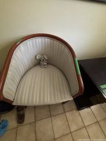 Front view of barrel accent chair showing beige and cream striped fabric upholstery with wooden frame and legs. Contains a small stuffed mouse on seat.