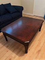 Overall view of rectangular solid wood coffee table with dark brown finish on hardwood floor next to navy sofa.