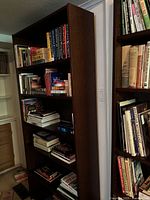 Side view of the dark brown wooden bookshelf loaded with books, showing depth and height against a white wall.