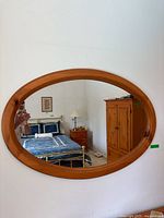Front view of the mirror hanging on a wall showing a bedroom reflected in the glass.