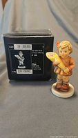 Figurine standing beside original black Goebel box with barcode labels visible