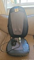 Front view of massage cushion on sofa with attached remote and power cord visible