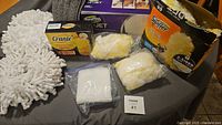 Cleaning accessories on table: chenille mop pads, Crante sponge pack, Swiffer duster refills