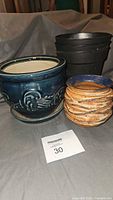 Group shot of all pots: blue ceramic, orange/blue ceramic, stacked black plastic pots with saucers