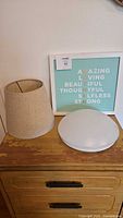 Wall art print standing on dresser beside lamp shade and LED ceiling light diffuser