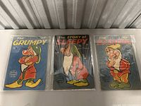 Three Disney Seven Dwarfs books from the 1930s: Grumpy, Sleepy and Bashful, displayed side by side in plastic sleeves.