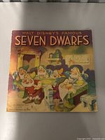 Front cover of the 1938 Walt Disney's Famous Seven Dwarfs book showing the dwarfs in a cottage scene.