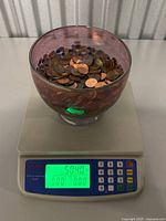 Glass bowl containing many copper pennies placed on a digital scale showing 5.04 pounds (about 2.29 kg).