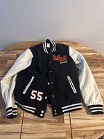 Full front view of black and white Disney Mickey Mouse bomber jacket laid flat on wooden table, showing patches and striped cuffs.